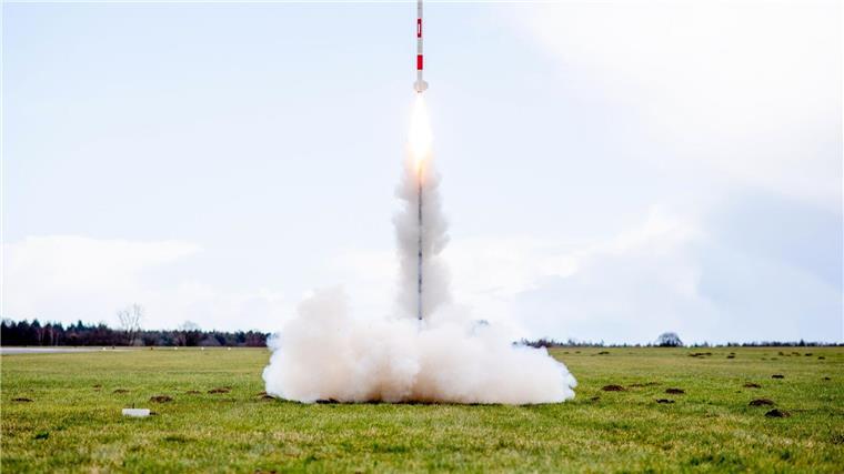 Eine mit mehreren Minisatelliten bestückte Rakete startet von einer Wiese auf dem Flugplatz.