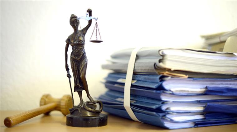 Eine modellhafte Nachbildung der Justitia steht neben einem Holzhammer und einem Aktenstapel.