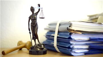 Eine modellhafte Nachbildung der Justitia steht neben einem Holzhammer und einem Aktenstapel.