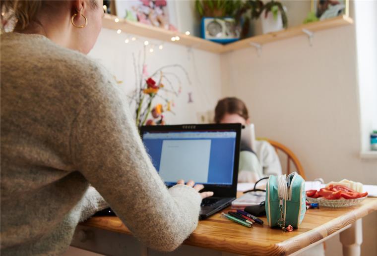 Eine Mutter arbeitet am Küchentisch, während ihre Tochter gegenüber in ein Tablet guckt. Nach Ansicht von Experten sollten Unternehmen darauf achten, dass nicht vor allem Frauen im Homeoffice arbeiten, während Männer im Büro bleiben.