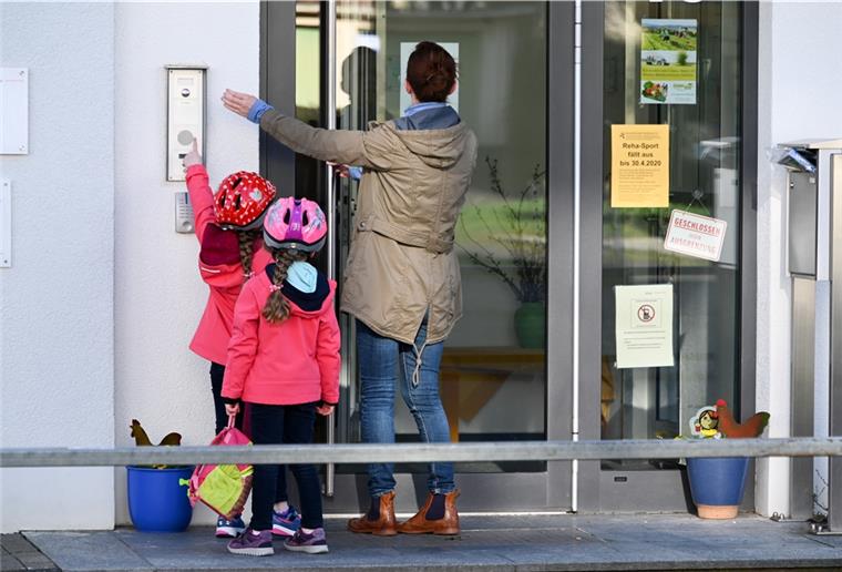 Eine Mutter steht mit ihren Kindern vor dem Kita-Eingang und klingelt.