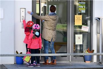 Eine Mutter steht mit ihren Kindern vor dem Kita-Eingang und klingelt.