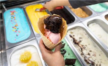 Eine Waffel wird in einer Eisdiele mit Eiskugeln verschiedener Sorten gefüllt.
