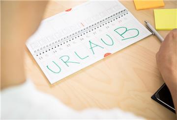 Ein Mann schaut in einen Terminkalender. Dort ist das Wort "Urlaub" in Großbuchstaben zu lesen.  Einfach so mehr Geld zum Urlaub? Das geht – wenn du Anspruch auf Urlaubsgeld hast. Wie du das herausfindest und warum auch Gewohnheit zum Recht werden kann.