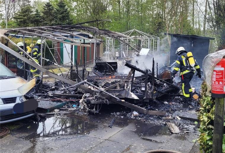 Einsatzkräfte der Feuerwehr während der Nachlöscharbeiten am völlig niedergebrannten Wohnwagen.