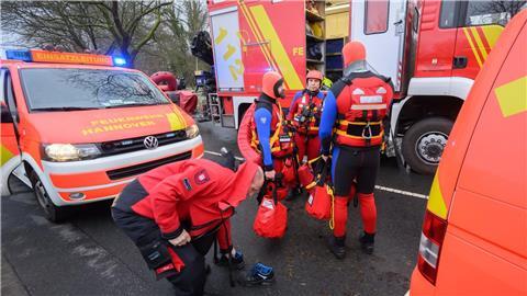 Einsatzkräfte der Wasserrettung der Feuerwehr stehen bei einem Einsatz auf einer überfluteten Straße.