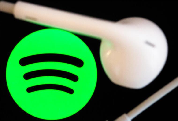  Kopfhörer liegen auf dem Bildschirm eines Smartphones, auf dem das Logo vom Musikstreaming-Dienst Spotify angezeigt wird. 