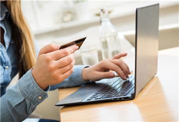Eine Person sitz am Laptop und hält eine Kreditkarte in der Hand. 