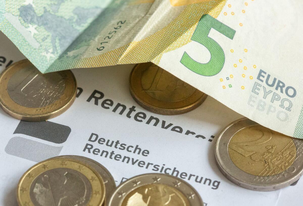  Münzen und eine Banknote liegen auf einer Renteninformation der Deutschen Rentenversicherung. 