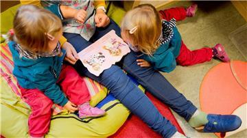 Erzieherin liest mit Zwillingen ein Buch.