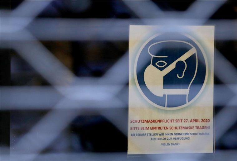 Ein Schild, das auf die Schutzmaskenpflicht in einem Geschäft hinweist, hängt hinter einem Gitter.