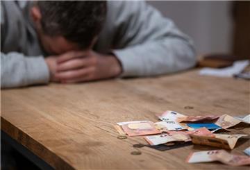 Ein Mann hat seinen Kopf auf seine Hände gelegt, während sich vor ihm Geldscheine, Münzen und Bankkarten auf einem Tisch befinden. (zu dpa: «Singles suchen häufiger Hilfe bei Schuldnerberatungen»)
