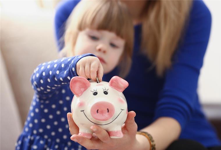 Mit Taschengeld umgehen lernen Kleines Mädchen steckt Münze in Sparschwein
