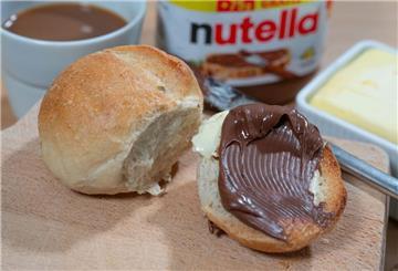Ein Brötchen mit Nutella liegt auf einem Frühstücksbrett. 
