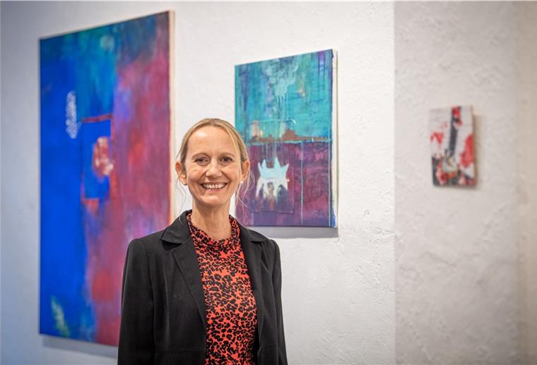 Frau steht vor einer Wand mit Acrylbildern und lächelt.