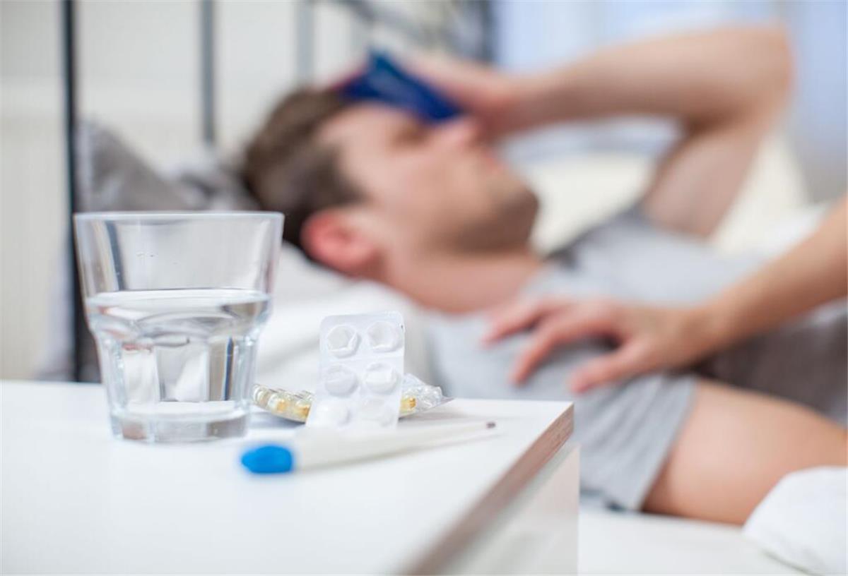 Kündigung wegen Krankheit? Wann Fehltage wirklich zum Problem werden Ein kranker Mann liegt im Bett. Auf dem Nachttisch steht ein Glas Wasser und liegen verschiedene Medikamente.