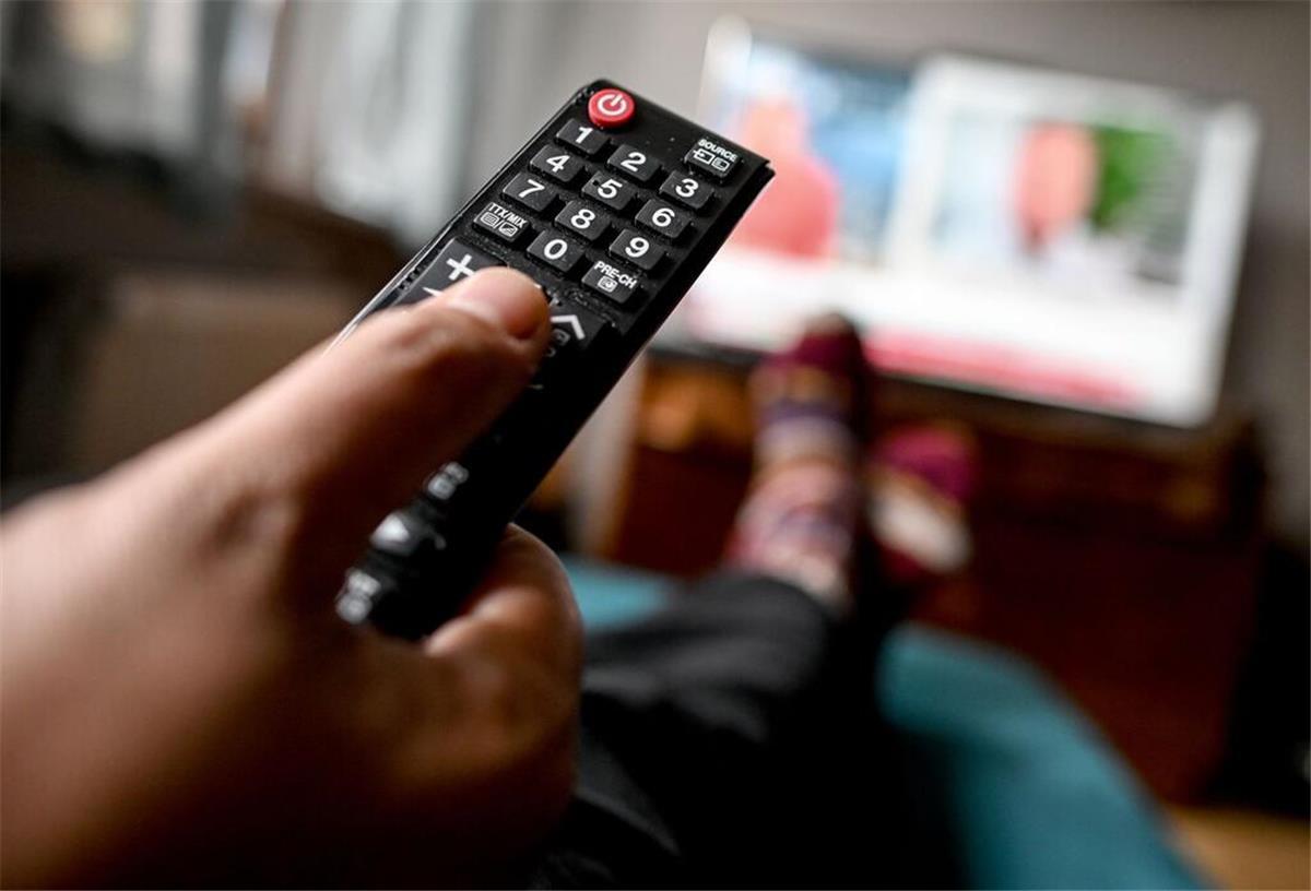 Streamingdienst erhöht Beitrag für Millionen Nutzer Eine Person hält eine Fernbedienung in der Hand und schaut Fernsehen.