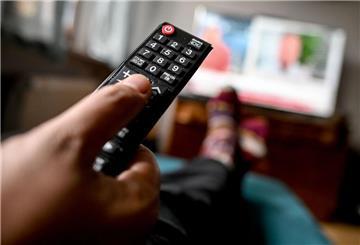 Eine Person hält eine Fernbedienung in der Hand und schaut Fernsehen. 