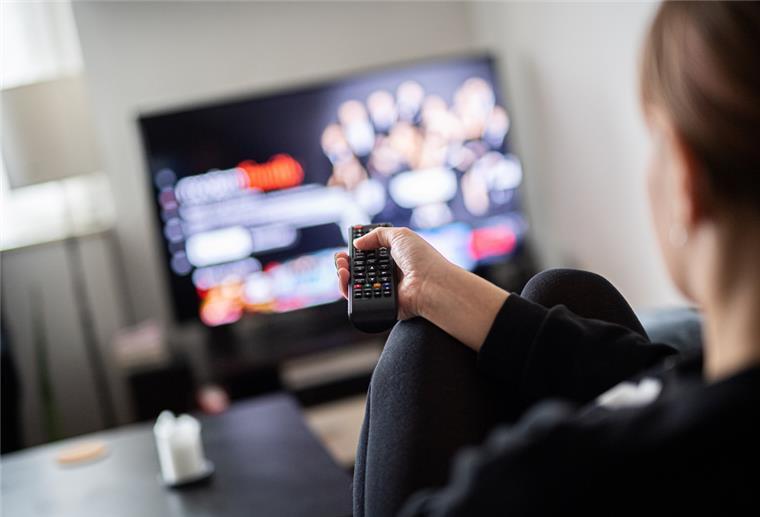  Eine Frau sitzt vor dem Fernseher und hält die Fernbedienung. 