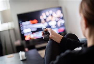  Eine Frau sitzt vor dem Fernseher und hält die Fernbedienung. 