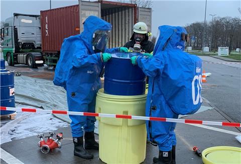 Feuerwehrleute in spezieller Ausrüstung hoben das beschädigte Fass in ein größeres Fass. 