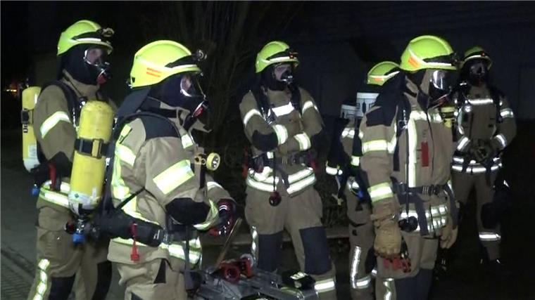 Feuerwehrleute mit Atemschutzmasken stehen vor dem Mehrfamilienhaus in Ronnenberg.