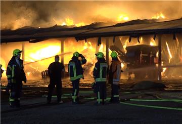 Feuerwehrleute stehen vor der brennenden Lagerhalle.