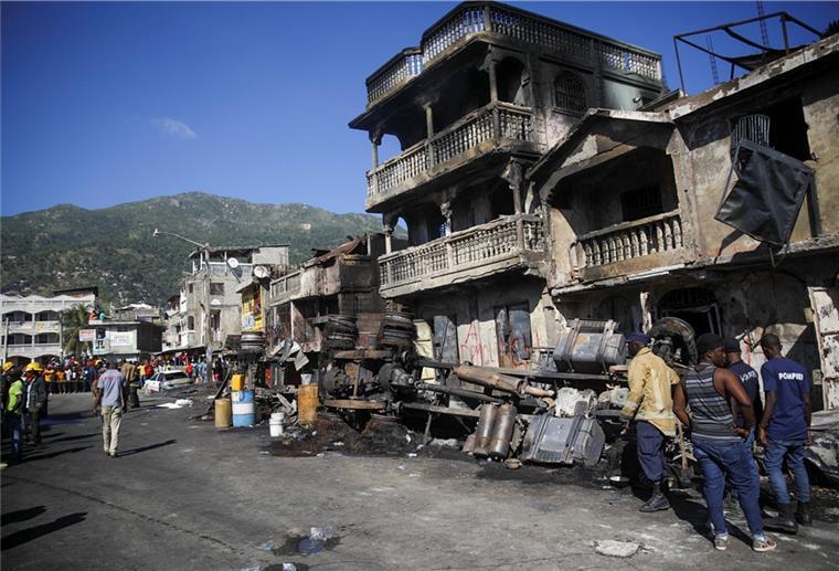 Feuerwehrleute stehen in Haiti neben den Überresten eines mit Benzin beladenen Lastwagens, der in Brand geriet und explodierte.