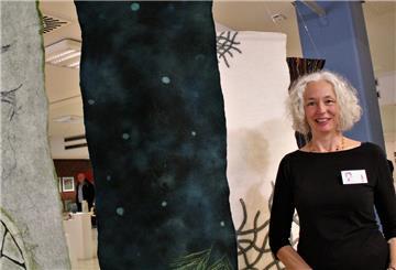 Eine Frau mit grauen Haaren steht vor einem Kunstwerk aus Filz.