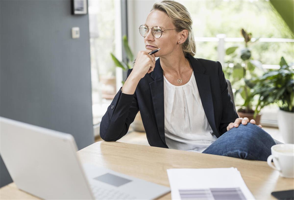 Finanzielle Unabhängigkeit: Warum Frauen mehr investieren sollten Eine Frau an einem Schreibtisch denkt nach.