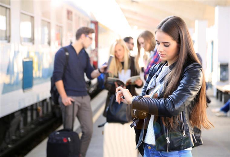 Eine Frau steht am Bahnhof und schaut auf die Uhr.