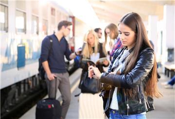 Eine Frau steht am Bahnhof und schaut auf die Uhr.