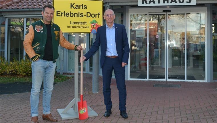 Zwei Männer stehen neben einem Schild und halten einen roten Spaten.