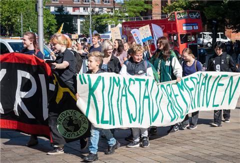 Eine Teilnehmerin eines Protestzugs der Klimabewegung Fridays for Future trägt ein Pappschild mit einer Darstellung, auf der ein Radfahrer ein Auto in einer Mülltonne entsorgt. Die Demonstration durch Lüneburg soll unter anderem auf die Notwendigkeit der Bahn-Neubaustrecke Hamburg-Hannover aufmerksam zu machen. +++ dpa-Bildfunk +++