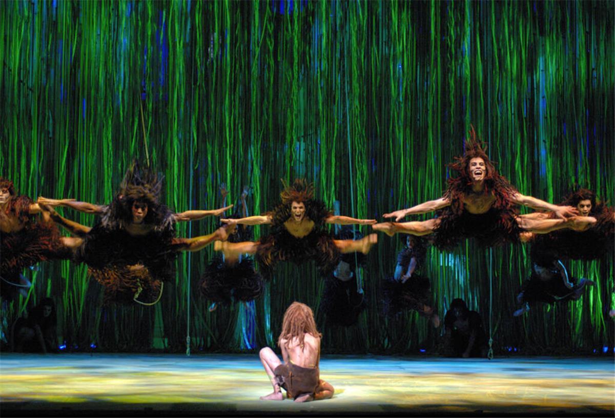 Junge Talente aufgepasst: Tarzan-Casting in Hamburg Ein Tarzan-Darsteller kniet auf der Bühne. Vor ihm springen weitere Darsteller in die Luft.