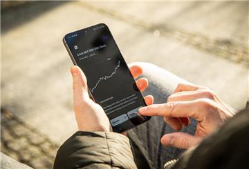 Ein Mann hält ein Smartphone in der Hand, auf dem der Kurs eines ETFs zu sehen ist.