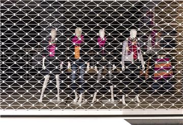 Puppen stehen im Schaufenster eines verriegelten Geschäfts.