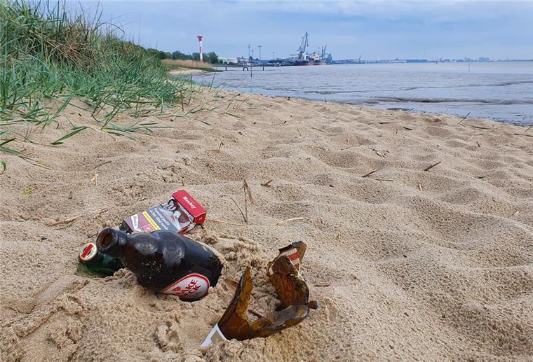 Glasflaschen und eine Zigarettenschachtel liegen am Nordenhamer Weserstrand im Sand.