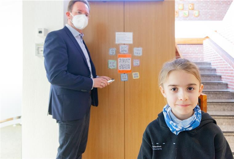 Gemeinsam mit Bürgermeister Marcus Itjen klebt der Viertklässler Karl die ersten QR-Codes mit den Kinderrechtsvideos gut sichtbar im Nordholzer Rathaus fest.