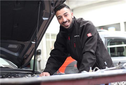 Ein junger Mann steht an einer geöffneten Motorhaube eines Autos.