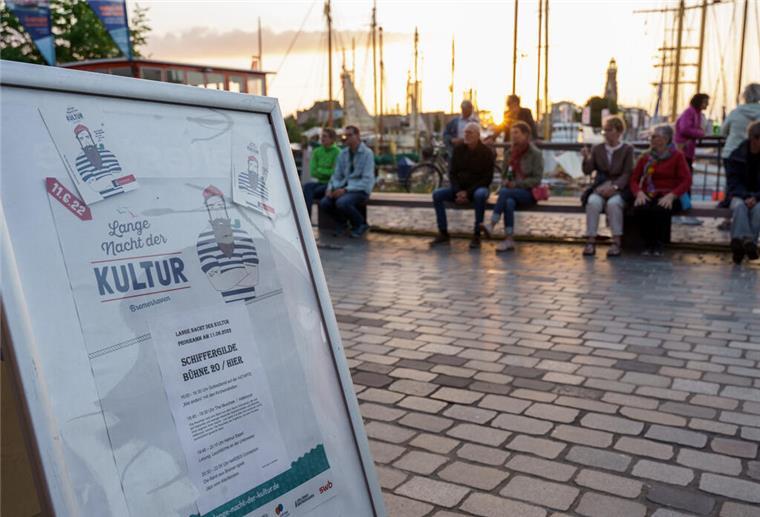 Lange Nacht der Kultur in Bremerhaven Ein Plakat der Langen Nacht der Kultur Bremerhaven. Im Hintergrund sitzen Menschen bei Sonnenuntergang.