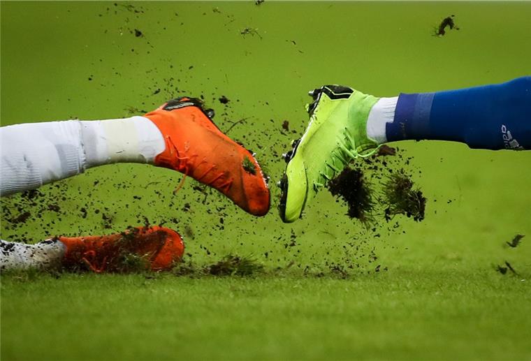 Gras fliegt um die Fußballschuhe zweier Spieler bei einem Zweikampf.