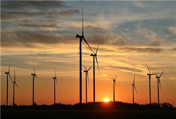Windräder in der Dämmerung. Die Sonne ist am Horizont zu sehen und erleuchtet den Himmel rötlich.