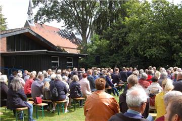 Gut 200 Menschen wohnten dem Gottesdienst bei, der am Sonntag im Pfarrgarten stattfand. Im Hintergrund die vom Feuer beschädigte Kirche. 