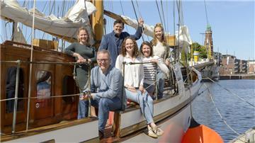 Mehrere Menschen stehen lächelnd auf einem Boot im Becken des Neuen Hafens Bremerhaven. 