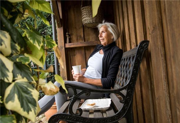 Eine Frau sitzt im Garten auf einer Bank.