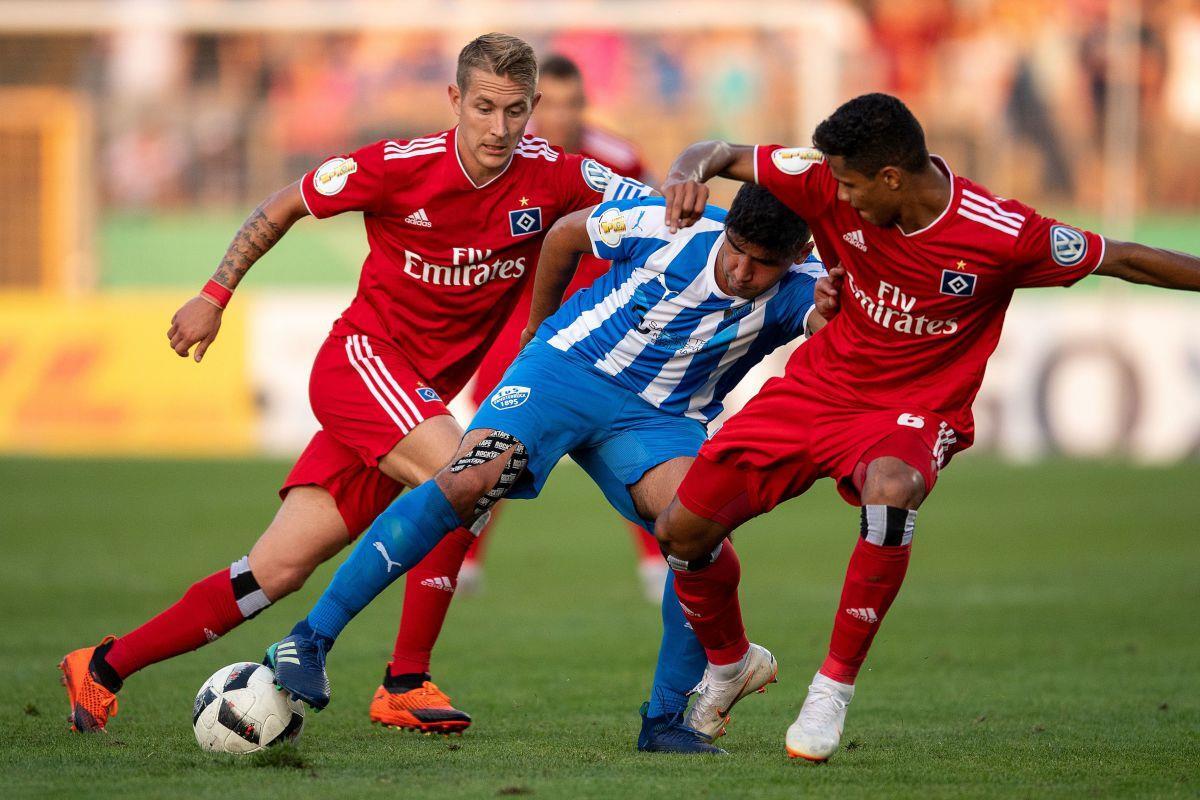 Hamburgs Lewis Holtby (l) und Douglas Santos (r) kämpfen mit Erndtebrücks Murat-Kaan Yazar um den Ball.