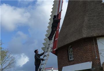 Handwerker erklimmen die Mühle, um ein Windbrett nach dem anderen einzusetzen.