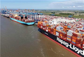 Zwei große Containerschiffe der Reedereien Maersk und Hapag-Lloyd liegen nebeneinander am Kai eines Containerterminals. Im Hintergrund sind zahlreiche Kräne und Containerstapel sowie eine weite, flache Küstenlandschaft zu sehen.
