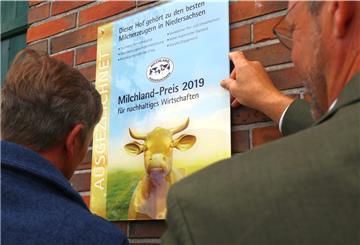 Hartwig Gloystein (links) und Jan Heusmann, Vorstand der Landesvereinigung Milchwirtschaft in Niedersachsen, montieren die Auszeichnung am Stallgebäude.